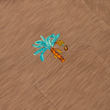 An extreme close-up shot of the left chest pocket area on the Baja Llama La Republica Embroidered Pima Slub Pocket Tee, highlighting the detailed brown slub fabric texture and an embroidered turquoise and orange banana tree with a hanging bunch of bananas.