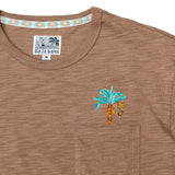 A close-up shot of the neckline and chest area on the Baja Llama La Republica Embroidered Pima Slub Pocket Tee, showing the brown textured fabric, a stitched pocket with an embroidered teal banana tree, and a geometric pattern on the inner collar.