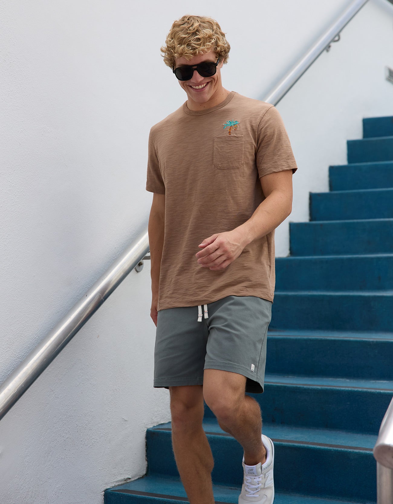 Smiling man walking near blue outdoor steps wearing Baja Llama La Republica Embroidered Pima Slub Pocket Tee
