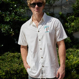 Man wearing white short-sleeve button-up shirt with embroidered palm tree pocket design outdoors