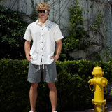 Full-length view of a model wearing a white 7-Seas relaxed fit button-up shirt and gray shorts standing outdoors next to a yellow fire hydrant