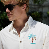 Close-up of model wearing white 7-Seas button-up shirt featuring embroidered chest palm tree design and sunglasses