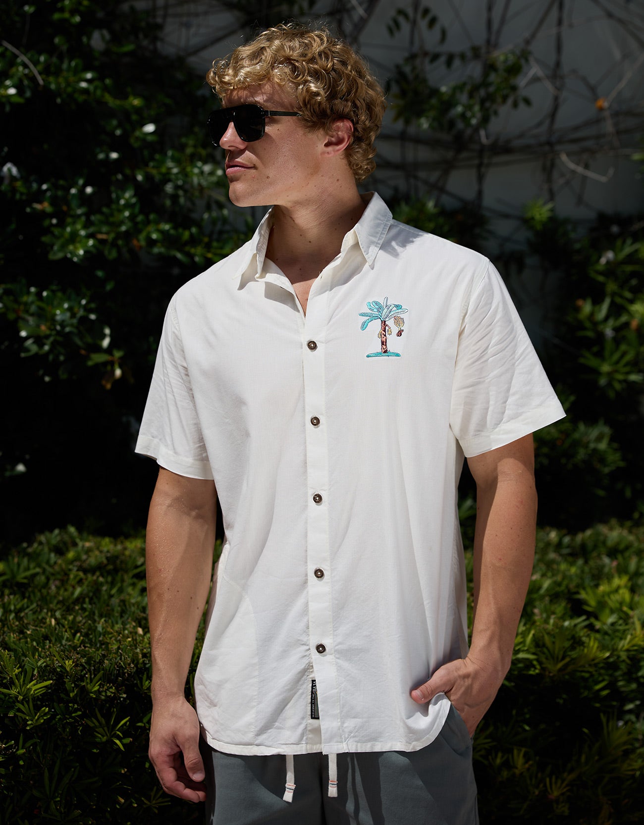 Model wearing white short-sleeve 7-Seas relaxed fit button-up shirt with chest embroidery and sunglasses outdoors