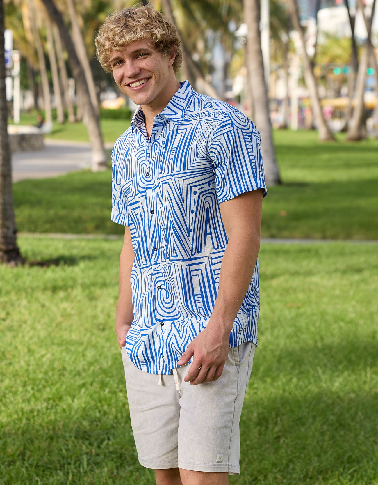 Model wearing blue and white geometric Line Work Mojave perforated short-sleeve button-up shirt in a park setting