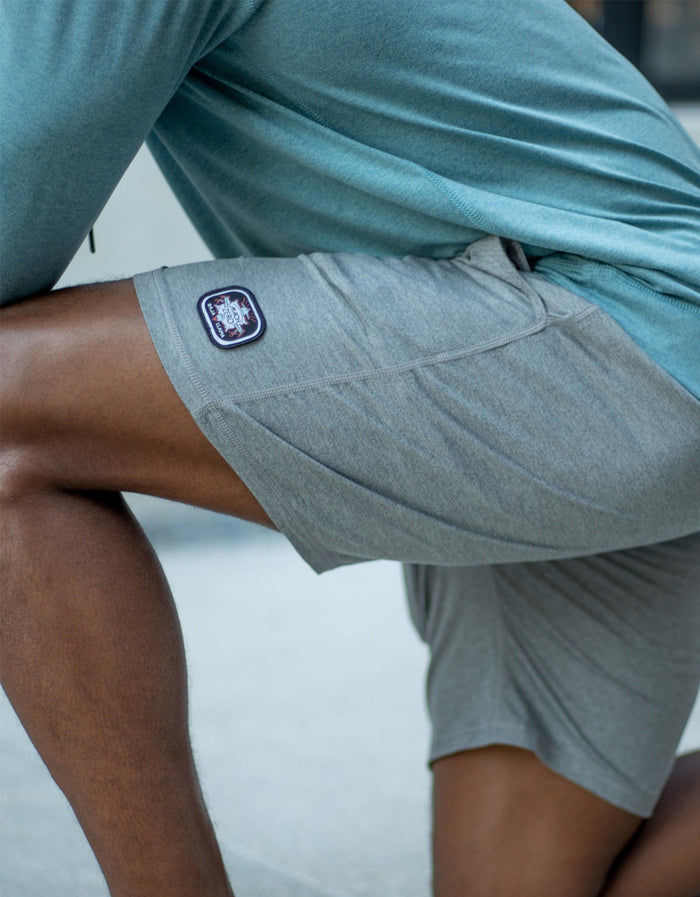 Close-up side view of a model kneeling while wearing the Baja Llama Mach Zero Lounge Shorts in gray, highlighting the branded patch.
