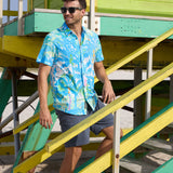 Model standing on green and yellow beach lifeguard tower stairs wearing Pastel Paradise reverse print blue and green perforated button-up shirt
