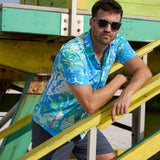 Model leaning on yellow lifeguard stairs wearing Pastel Paradise reverse print blue and green perforated button-up shirt and sunglasses