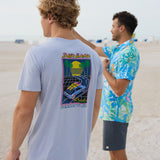 Model wearing Baja Llama Radical Misadventurist purple acid wash graphic tee showing back print on the beach with another model in background