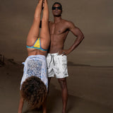 Person wearing Desert Martians men’s 8 inch inseam stretch performance black and white shorts with sunglasses by the ocean.