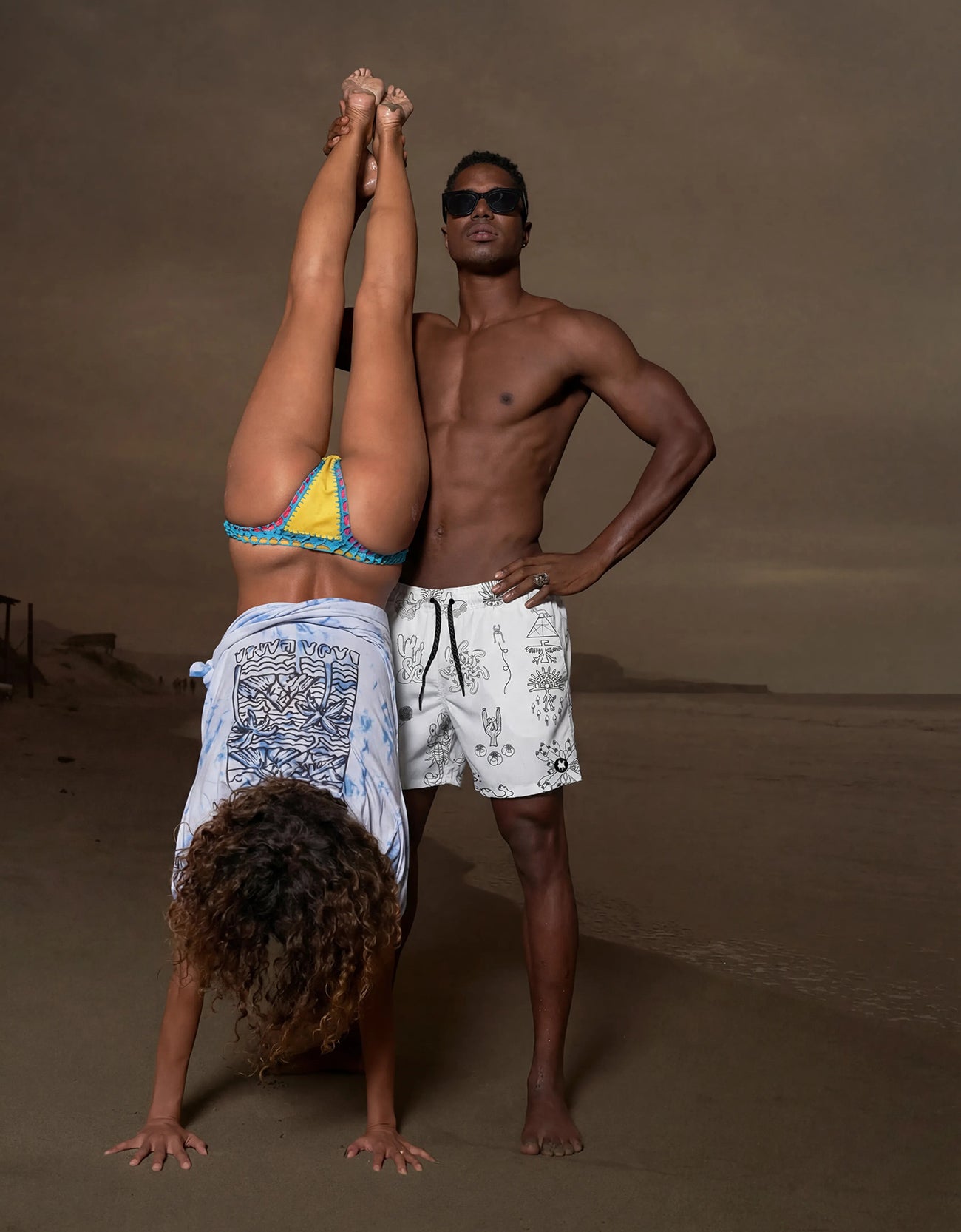Person wearing Desert Martians men’s 8 inch inseam stretch performance black and white shorts with sunglasses by the ocean.