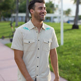 Smiling model walking in a park wearing the Baja Llama Reptile Wrangler cream western button-up shirt with embroidered gecko shoulder details