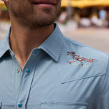 Close-up of the Baja Llama Road Runner blue western snap button-up shirt showing detailed road runner shoulder embroidery and turquoise-accented buttons