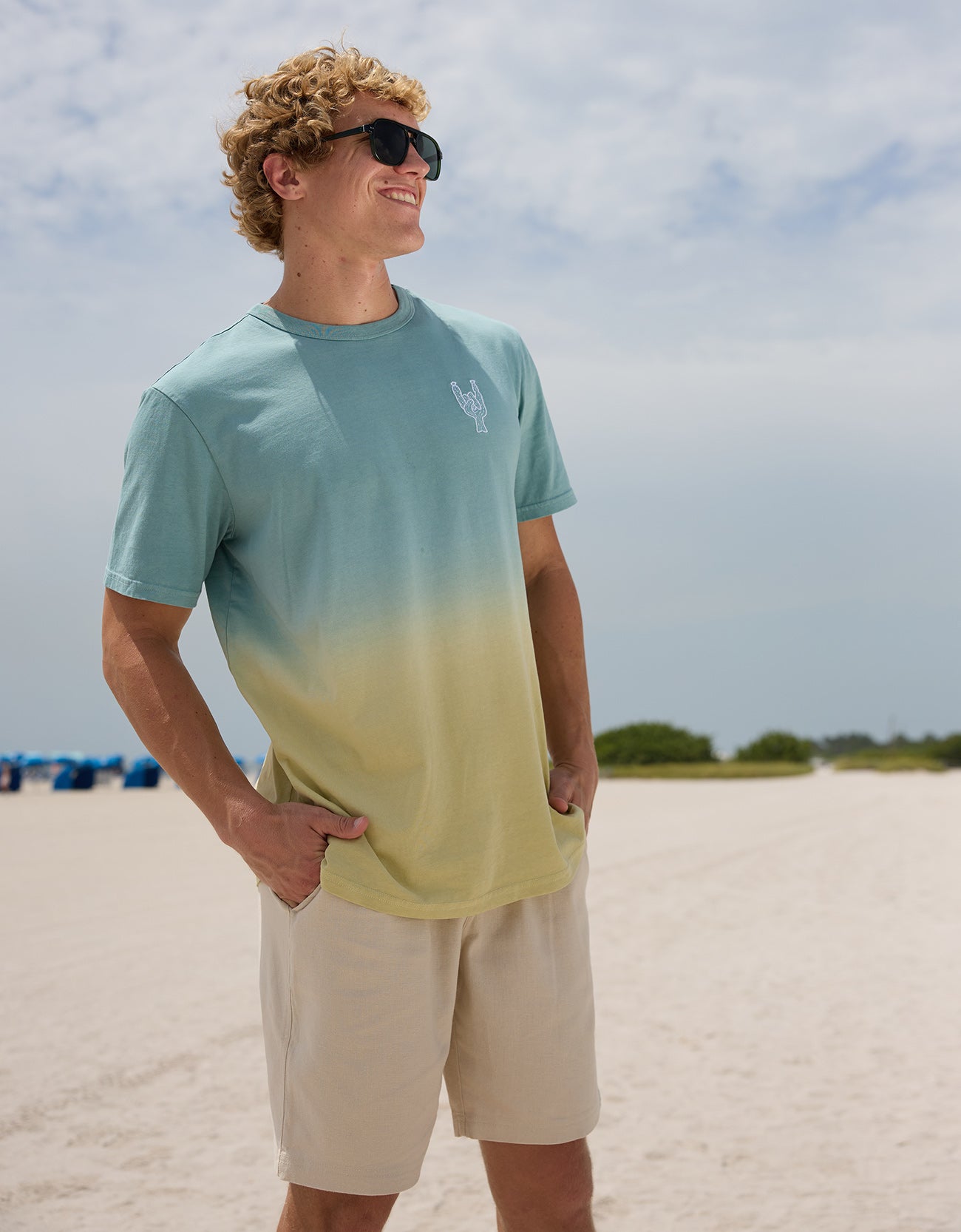 Model wearing the Baja Llama Rock On Cactus embroidered ombre heavy tee and sunglasses on a sunny beach