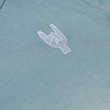 Close-up of the left chest on the Baja Llama Rock On Cactus Embroidered Primo S.E. Heavy Tee, showcasing the small white embroidered rock-on sign cactus against the teal-blue upper section of the shirt.