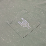 Close-up of the front chest pocket on the Baja Llama Greatful Dyed Rock On Cypress Green Heavy Tee, showing a white embroidered cactus in the shape of a rock-on sign