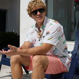 Model sitting outdoors wearing sunglasses and the Baja Llama The BBQ Shirt white relaxed-fit button-up with playful cookout and summer print graphics