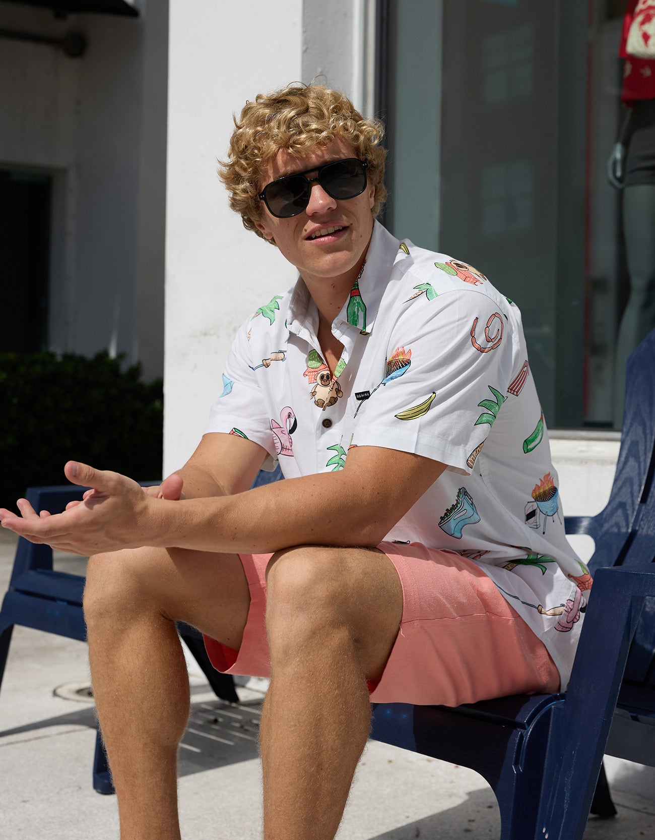 Model sitting outdoors wearing sunglasses and the Baja Llama The BBQ Shirt white relaxed-fit button-up with playful cookout and summer print graphics