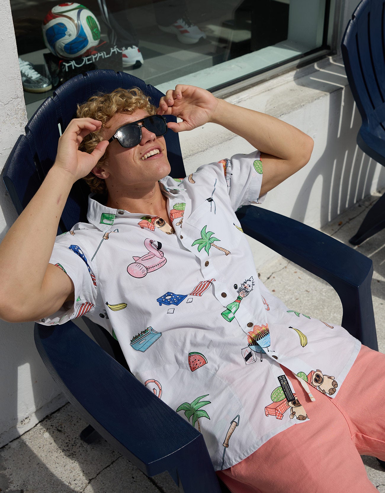 Model wearing Baja Llama The BBQ Shirt 7-Seas relaxed fit button-up and sunglasses while relaxing in a chair.