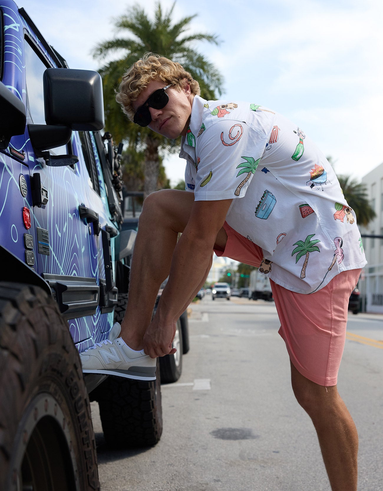 Baja Llama The BBQ Shirt 7-Seas Relaxed Fit Button Up white short sleeve shirt worn by a model tying his shoe next to a truck.
