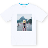 Front flat-lay view of the Baja Llama The Girl In Ipanema Primo Graphic Tee, featuring a white short-sleeve t-shirt with a large rectangular photographic print on the center chest depicting a woman in a swimsuit near Ipanema Beach.