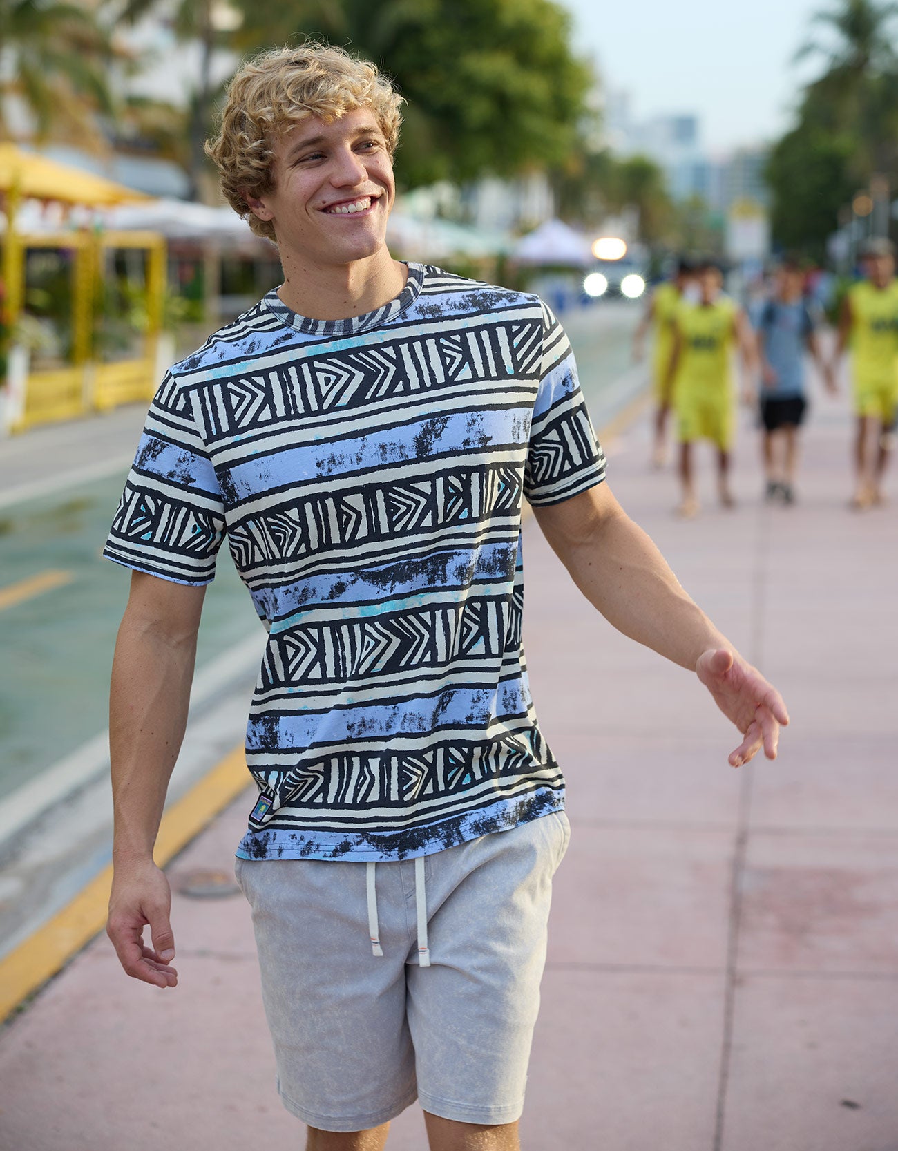 Smiling male model walking along a sunny outdoor boardwalk wearing The Good Ol’ Days patterned heavy tee by Baja Llama