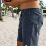 Baja Llama Too Easys Dark Slate Stretch Cotton Shorts close-up view of side pockets, drawstring waistband, and hem logo on a beach.